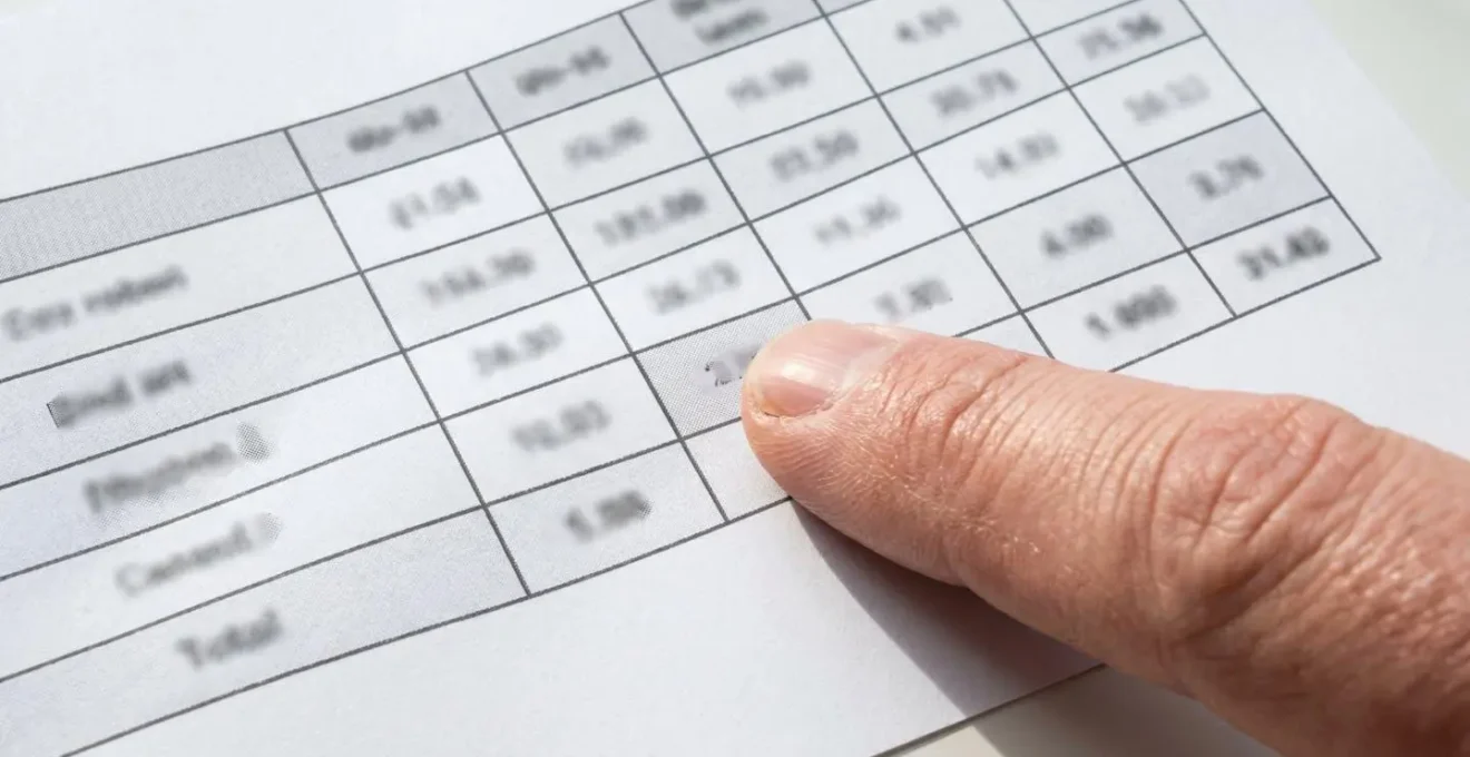 Primer plano de una mano adulta señalando con el índice una celda específica de una tabla comparativa impresa sobre papel blanco