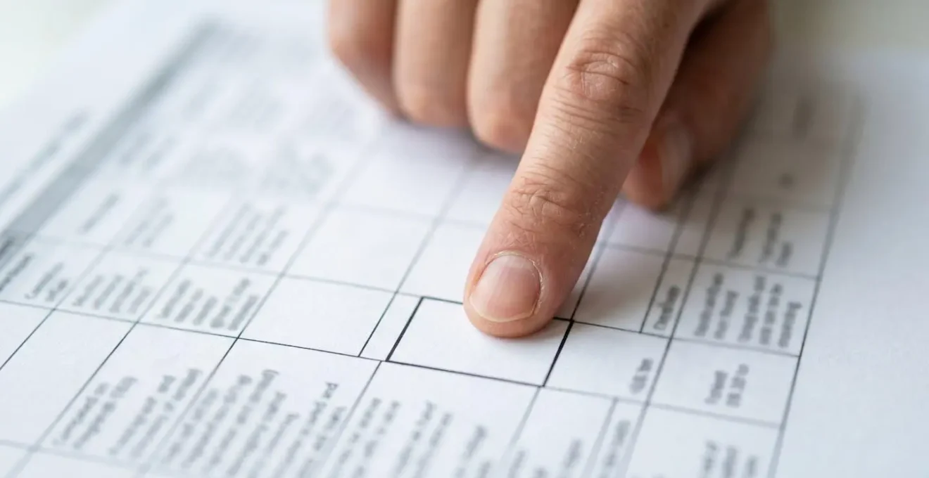 Primer plano de una mano adulta señalando con el índice una celda específica de una tabla comparativa impresa sobre papel blanco
