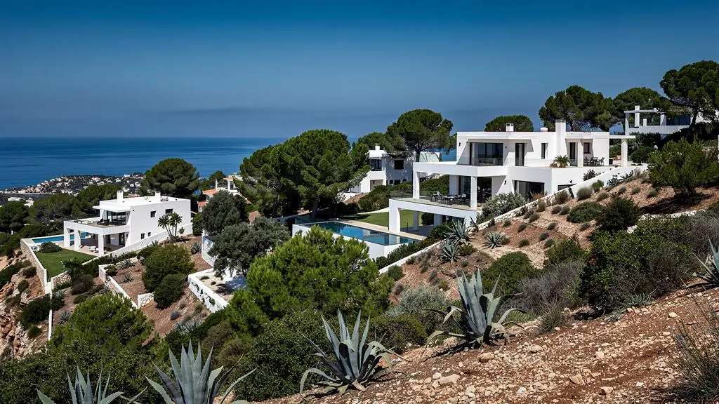 Vista amplia de un barrio residencial de lujo en ladera en Ibiza mostrando arquitectura mediterránea blanca y paisaje natural Vista amplia de un barrio residencial de lujo en ladera en Ibiza mostrando arquitectura mediterránea blanca y paisaje natural